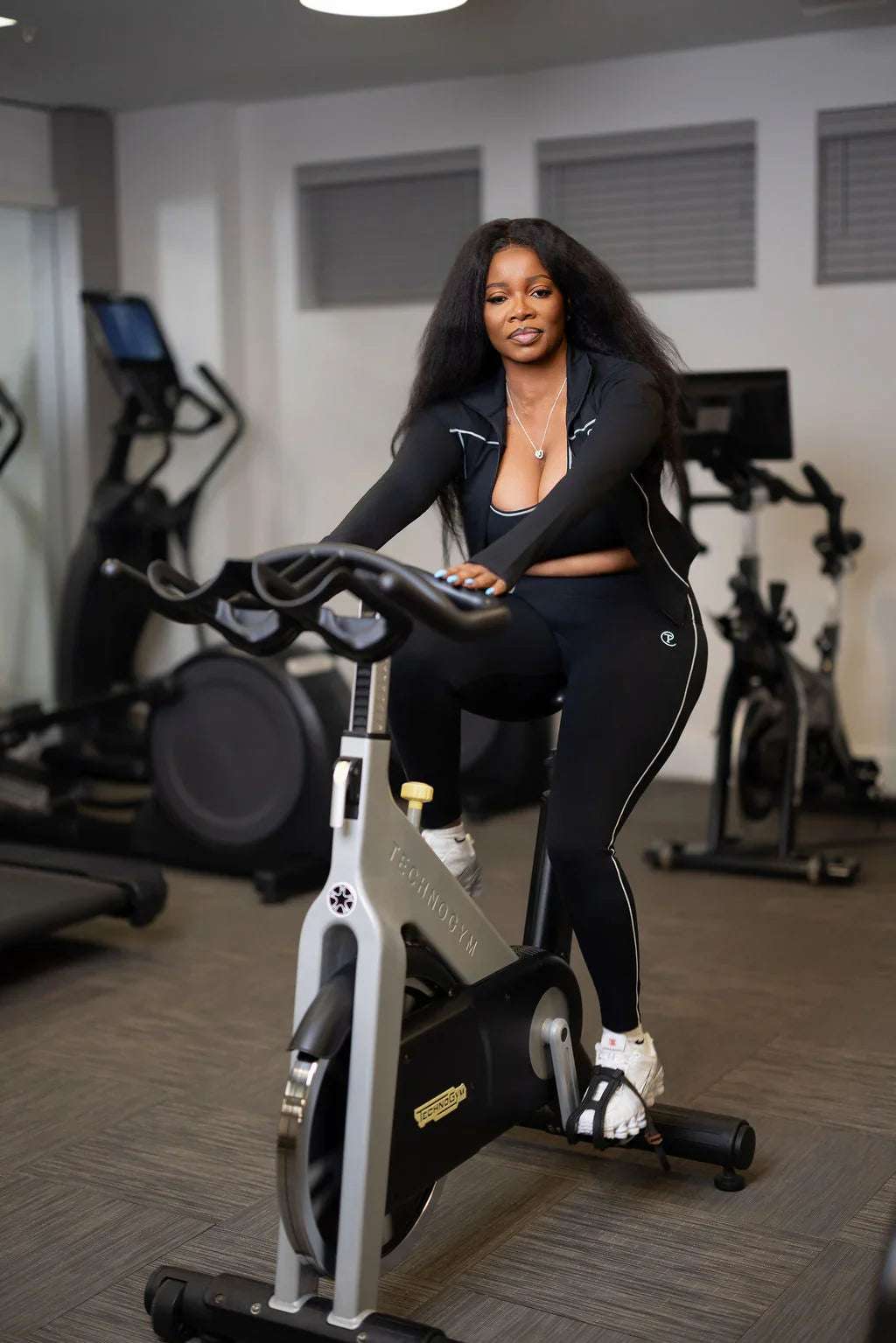 Woman in black athletic wear on stationary bike in modern fitness gym