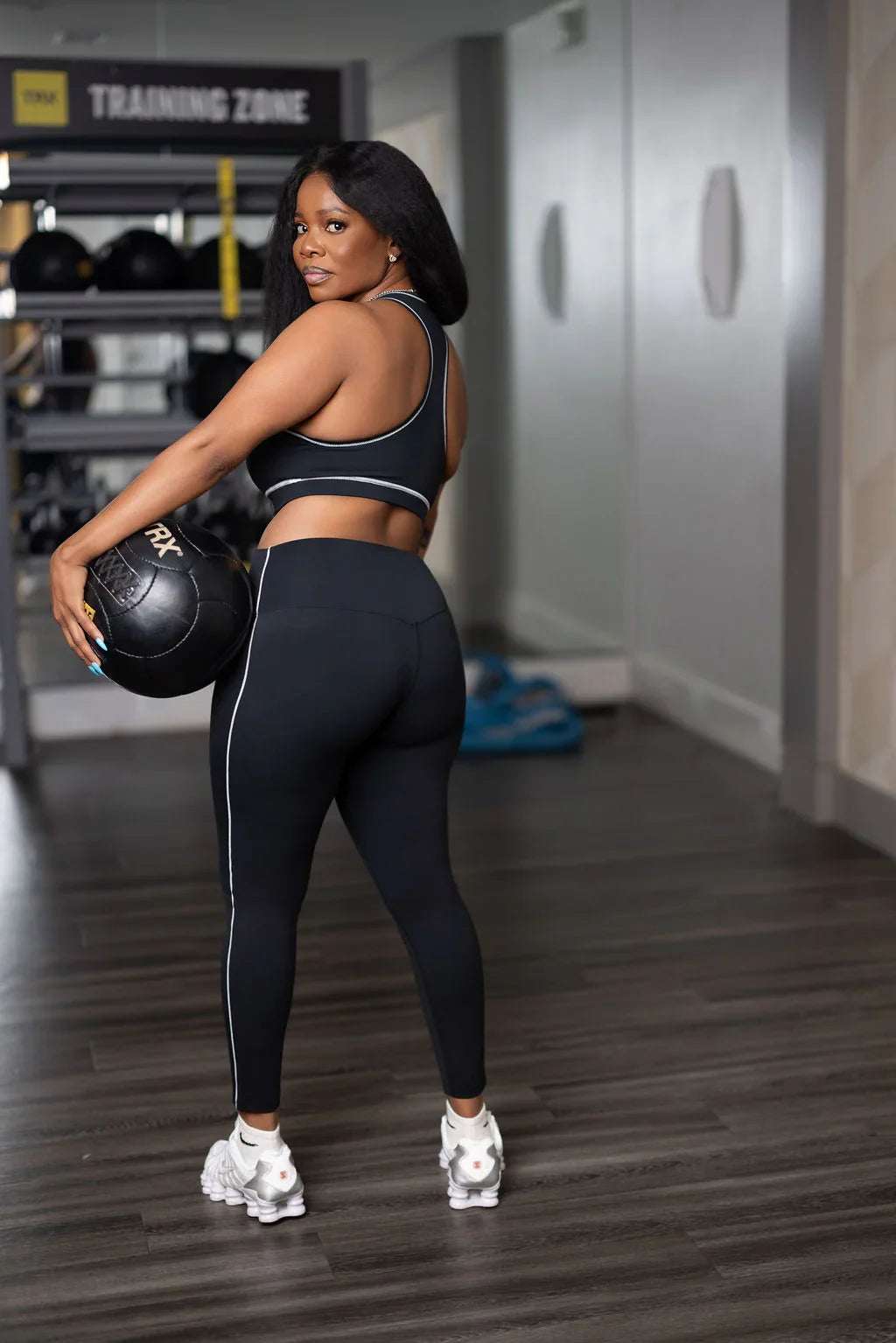 Woman in black athletic leggings and sports bra holding medicine ball in gym