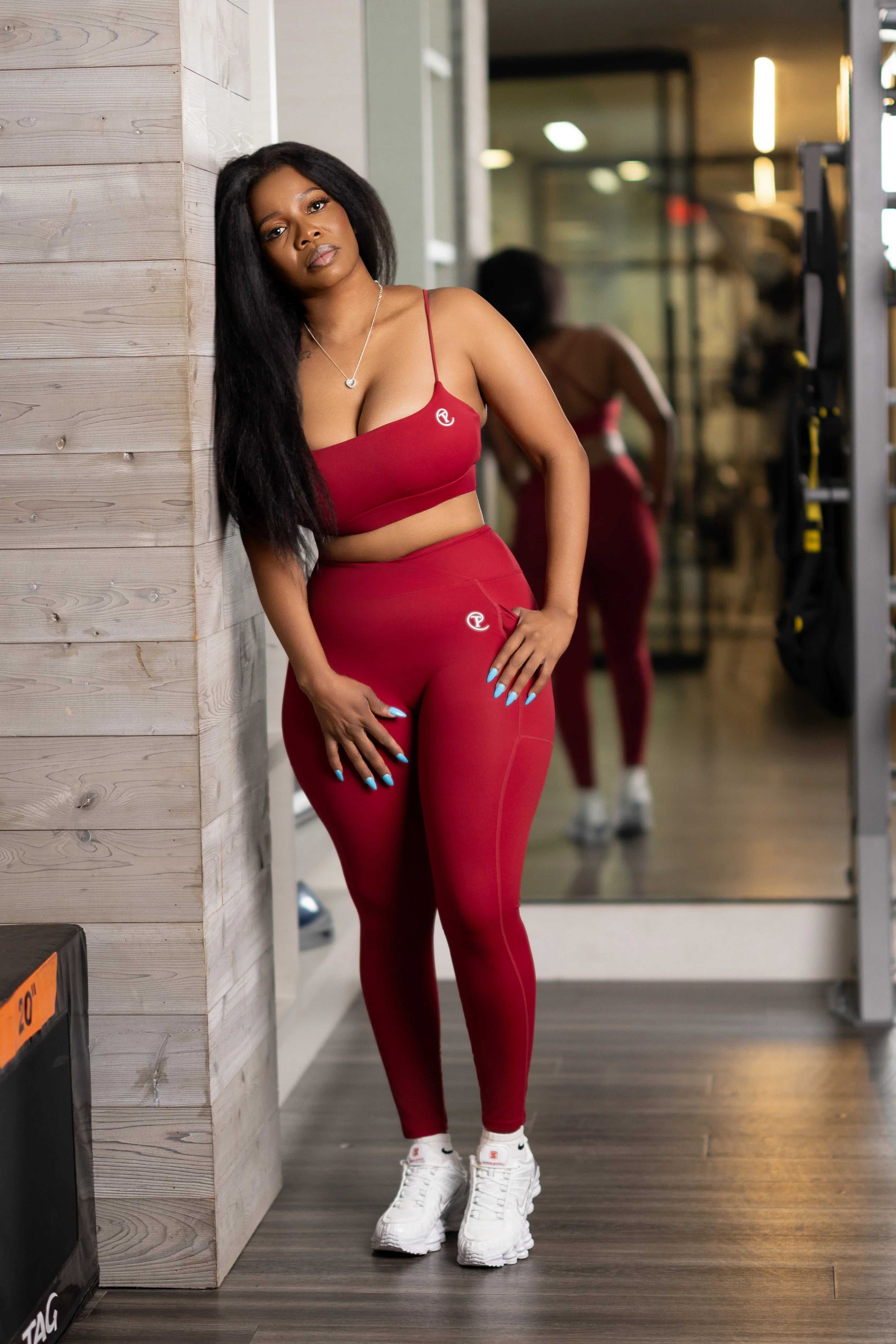 Woman in red matching sports bra and leggings set with white sneakers posing in gym