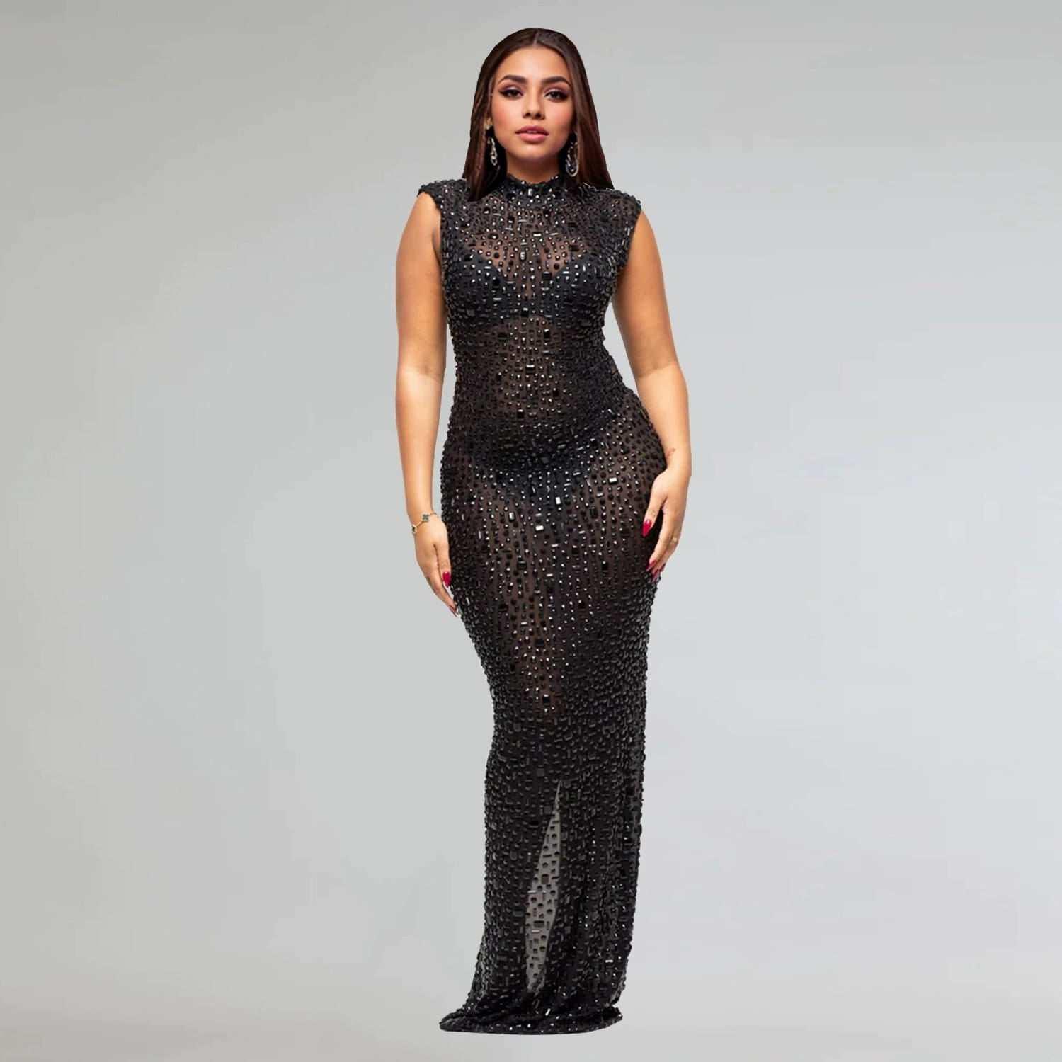 Woman in a black sheer embellished evening gown posing against a plain background