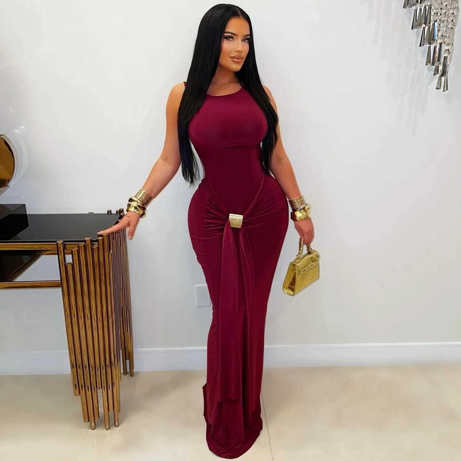 Woman in a sleeveless burgundy bodycon evening gown with gold accessories, holding a gold purse