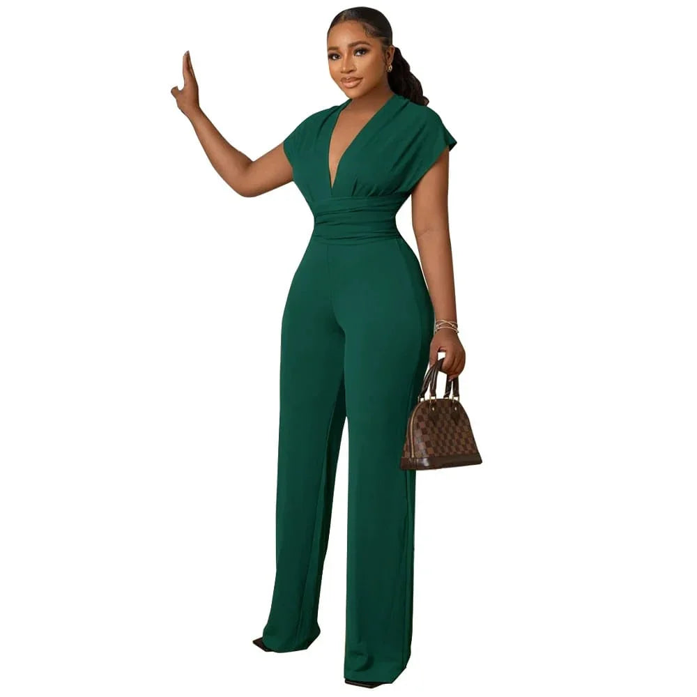 Woman in elegant green jumpsuit with deep V-neck, holding a brown checkered handbag