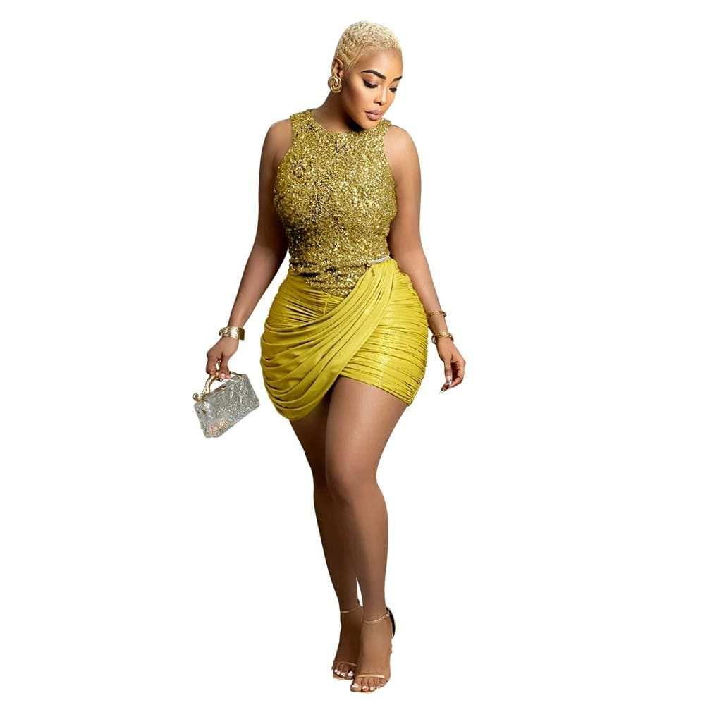 Woman in gold sequin sleeveless mini dress with draped skirt, holding a glittery purse
