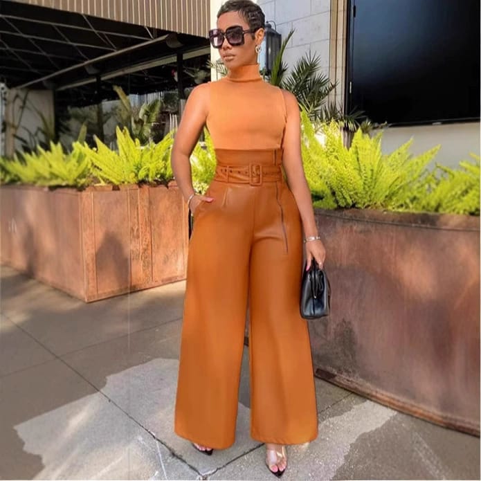 Woman in sleeveless orange turtleneck top and wide-leg high waist pants, holding a black purse