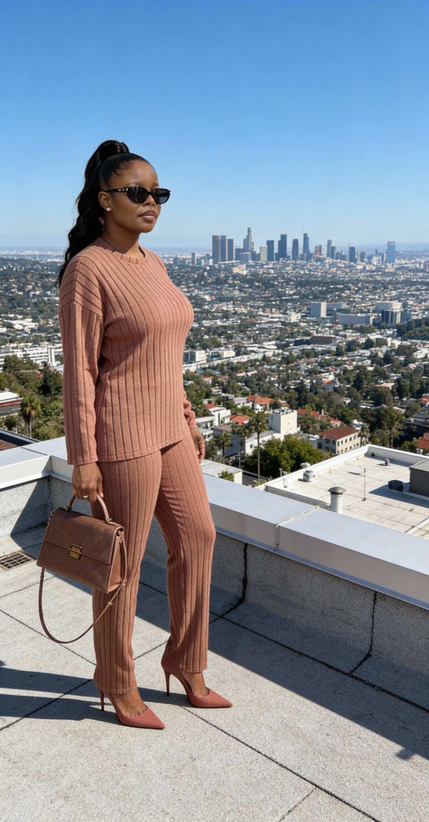 Woman in ribbed knit matching set with handbag and heels, city skyline in background