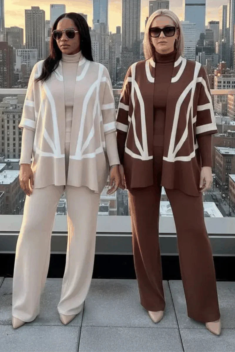 Two women in stylish wide-leg pantsuits with geometric jackets, standing on a rooftop city view.