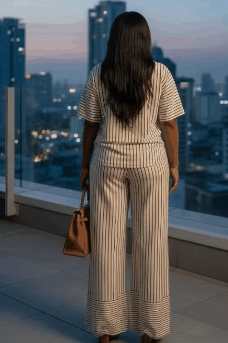 Woman in striped lounge set with brown handbag on city balcony at sunset