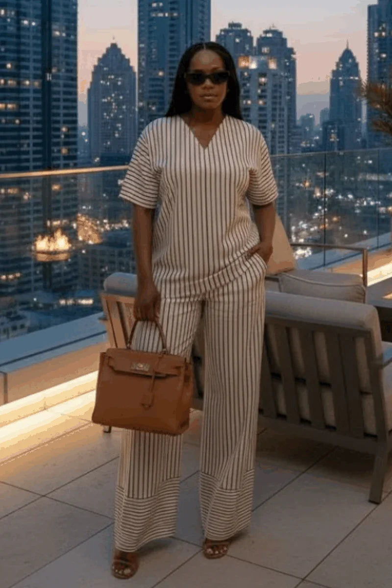 Woman in striped two-piece outfit with wide-leg pants and brown handbag on city rooftop at dusk
